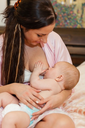 Young mum nurses the child on  on the house bed. Breastfeeding.