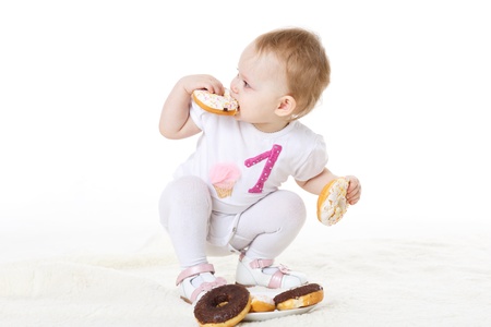 Little messy child eating doughnuts on a white background.