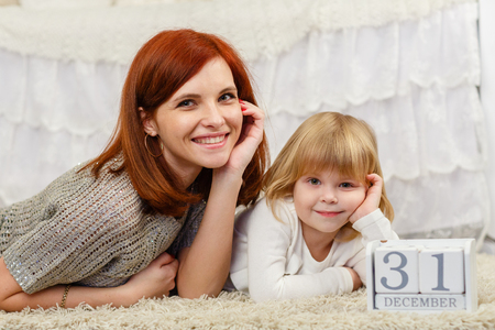 Happy mother and sweet little daughter with date 31 december are lying on the carpet in the room . Eve of New Year.の写真素材