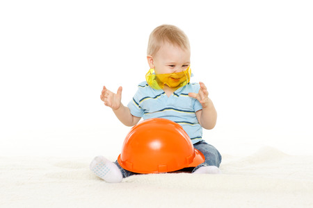 Little child plays with orange construction protective helmet and huge yellow protective eyeglasses on a white background. Profession - future builder.の写真素材