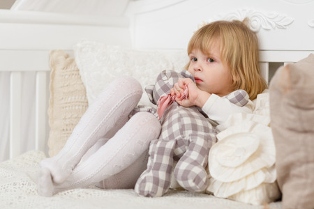 Sad pretty girl with toy bear sits on a sofa in the room.の写真素材