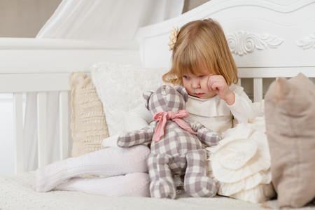Sad pretty girl with toy bear sits on a sofa in the room.の写真素材