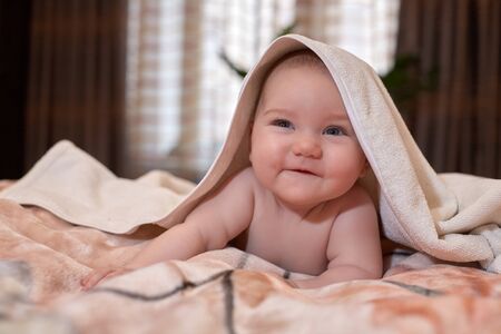 Sweet small baby with  towel lies on the bed at home.の写真素材