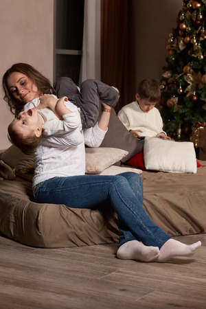 Happy family are playing on a bed near Christmas tree at home. Merry Christmas and Happy New Year. Beautiful young mother with two sons.の写真素材
