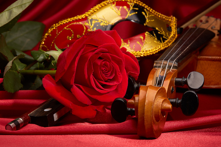Violin (fiddle), theater mask and red rose lying on the perfect red satin fabric. String instrument.の写真素材