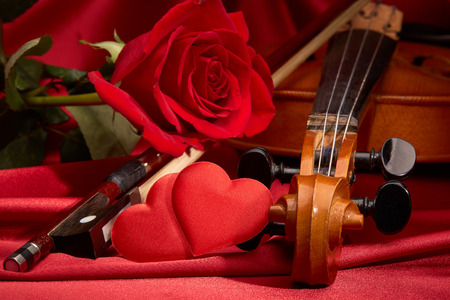 Violin (fiddle), red hearts and red rose lying on the perfect red satin fabric. String instrument. Valentine's day.の写真素材