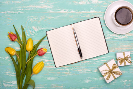 Bouquet of spring tulips flowers, gift boxes and blank daily log with fountain pen on a green wooden...