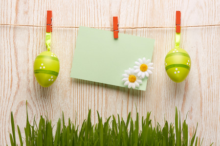 Colored easter eggs, spring green grass and empty sheet  on a wooden  background. Greeting card.の写真素材