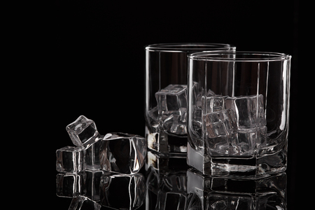 Two glasses for whiskey with ice cubes on black background.の写真素材