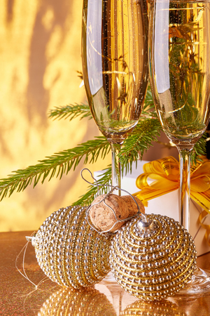 Two glasses with champange, fir tree branch, gift box and christmas toy on a gold background. New year and Christmas.の写真素材