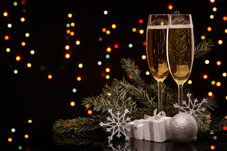 Two glasses with champange, fir tree branch with decoration, gift boxes on a black background with multi-colored lightes of garland.  New year and Christmas.の写真素材