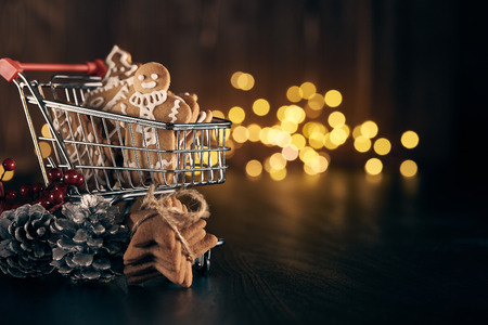 Shopping trolley with gingerbread cookies on a dark background with with LED lights garland. Christmas and New Year sale.の写真素材
