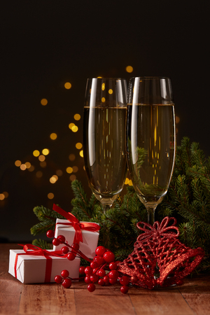Two glasses with champange, gift boxes, fir tree branch with decorations on a dark background with LED lights garland. New year and Christmas.の写真素材