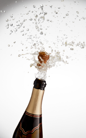 Explosion of splashing  sparkling wine with flying cork out of champagne bottle on a white backgroundの写真素材