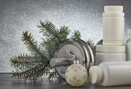 Sports nutrition (supplements), dumbbells, fir tree branches and christmas ormament on a grey background.  Horizontal view. New Year and Christmas. Fitness. Healthy lifestyle.の写真素材