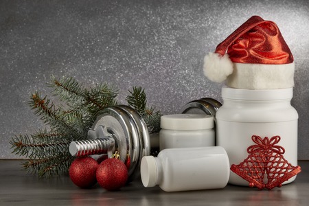 Sports nutrition (supplements), dumbbells, fir tree branches and christmas ormament on a dark background.  Horizontal view. New Year and Christmas. Fitness. Healthy lifestyle.の写真素材