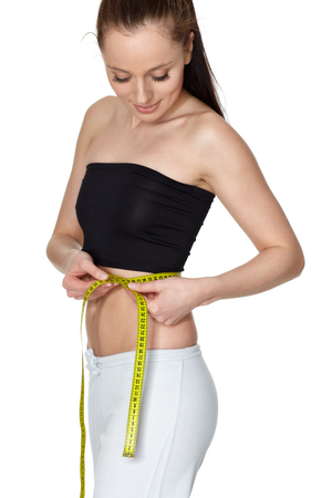 The beautiful young woman measures a volume of waist on a white background.  Concept of healthy lifestyle.の写真素材