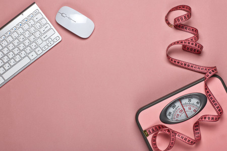 Female fitness still life. Scales, measuring tape, computer keyboard and mouse on pink background. Mockup. Planning of diet and trainings. Top view with copy space. Healthy lifestyle concept. Slimmingの写真素材