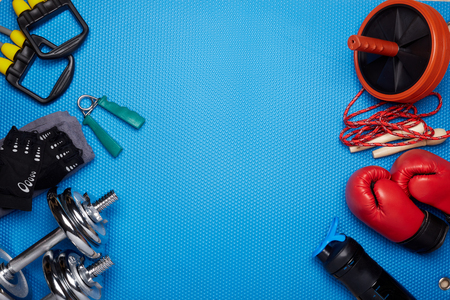 Sport accessories. Boxing gloves, dumbbells, skipping rope, sneakers, wheel exercise  on a blue background.  Top view with copyspace. Fitness, sport and healthy lifestyle concept.の写真素材