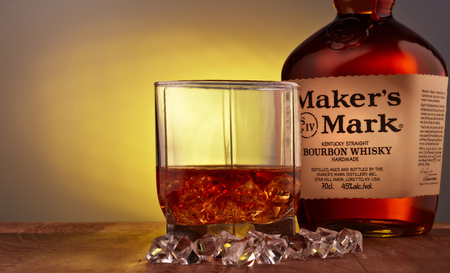 Bottle of Maker's Mark  kentucky straight bourbon whisky handmade and glass with drink and ice standing on a wooden table.のeditorial素材