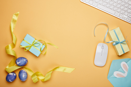 Colored easter eggs, gift box, computer keyboard and mouse, blank sheet with envelope on a yellow  background. Top view with copy space. Greeting card, Easter backgroundの写真素材