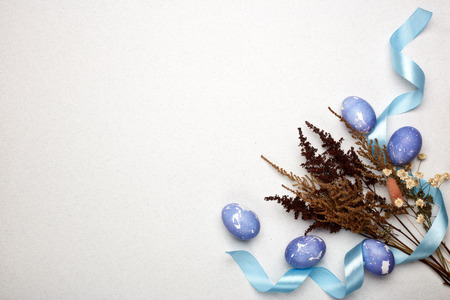 Colored easter eggs, flowers and ribbon on a lilac  background. Top view with copy space. Greeting...