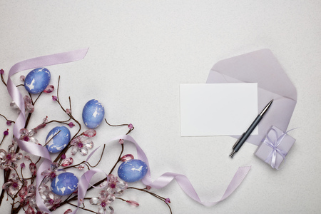 Colored easter eggs, gift box, decorative flowers and blank sheet with envelope  on a lilac  background. Top view with copy space. Greeting card, Easter backgroundの写真素材