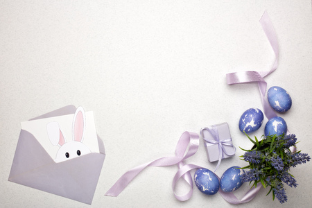 Colored easter eggs, gift box, decorative flower and blank sheet with envelope  on a lilac ...
