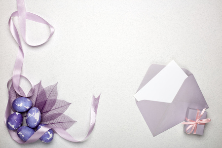 Colored easter eggs, gift box, decorative purple leaves and blank sheet with envelope  on a lilac ...