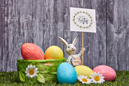 Colored easter eggs, easter rabbit and flowers lying on a green grass on a grey wooden  background...