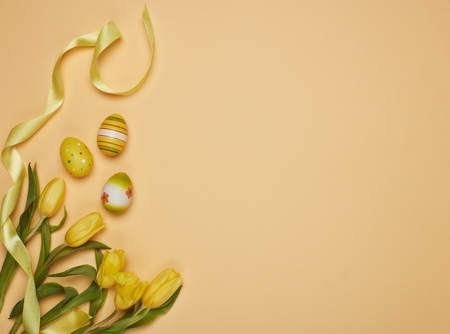 Colored easter eggs, spring tulips flowers and ribbon  on a yellow background. Top view with copy...