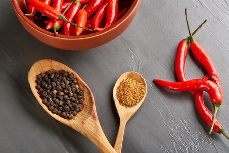 Still life with different peppers (whole black dry and powdered mix peppers in a wooden spoons, fresh red chile peppers in a bowl) on a gray background. Top view.の写真素材