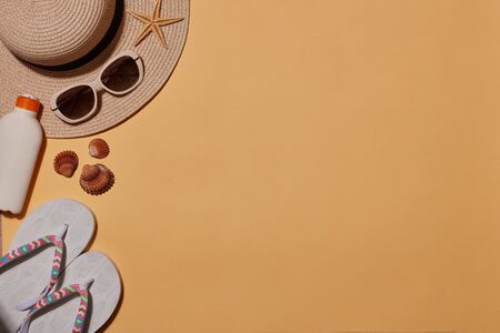 Beach accessories: white female flip flops, straw hat, sunglasses, sunscreen on yellow background....