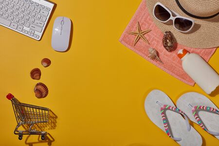Beach accessories, computer keyboard and shopping trolley  on yellow background. Top view with copy space. Concept of sea vacation and travel. Travel agency. Internet shop. Seasonal saleの写真素材