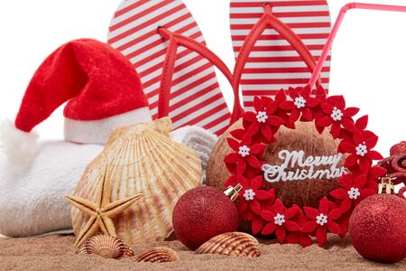 Still life with beach accessories (flip flops, towel, seashells, sand, coconut) and christmas ornaments on white background. Christmas. Winter  vacation  in warm countries, beach holidayの写真素材