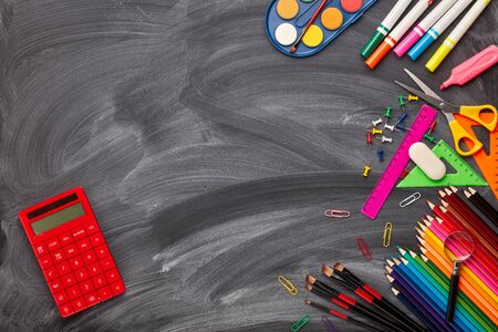Stationery accessories and calculator on background of school blackboard. Top view, copy space....