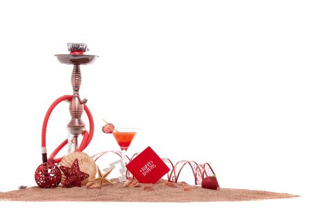 Festive beach still life: glass with cocktail, hookah (shisha), seashells, sand and christmas...
