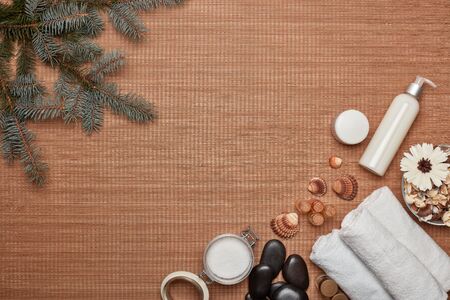 Spa still life with cosmetic creams, towel, stones for massage and fir branch on bamboo mat background. Top view with copy space. Healthy lifestyle, body care, Spa treatment. New Year and Christmasの写真素材