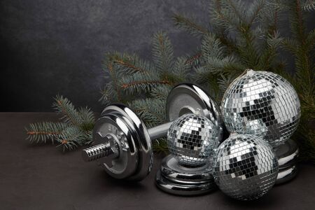 Sports equipment (dumbbell with weights), fir branch, Christmas ornament on dark grey background. Fitness, sport or healthy lifestyle concept. New Year and Christmas.の写真素材