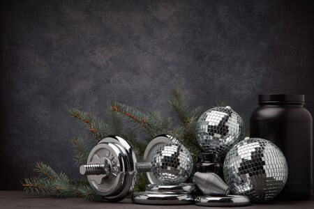 Sports nutrition (supplements), sports equipment, branch of fir,  Christmas ornaments on dark grey background with copy space. Fitness, sport or healthy lifestyle concept. New Year and Christmas.の写真素材