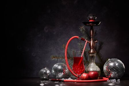 Hookah (shisha), mirror balls (disco ball), glass with cocktail, fir branch, red apples and ice on dark stone background with copy space. New Year and Christmas. Weekend or holiday party.の写真素材