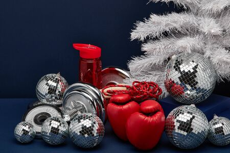 Dumbbell, boxing gloves, skipping rope, Christmas decoration on dark blue background with copy space. For design of advertising, web design. Christmas and New Year. Fitness, sport or healthy lifestyleの写真素材