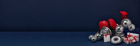 Dumbbell, boxing gloves, gift boxes and mirorr balls on dark blue background with copy space. For design of advertising, web design. Christmas and New Year. Fitness, sport or healthy lifestyle conceptの写真素材