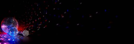 Glittering mirror disco balls and microphone on dark background with multicolor lighting. Copy...