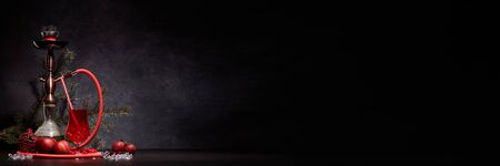 Hookah, glass with cocktail, fir branch, Christmas ornaments, red apples and ice on dark stone background with copy space. New Year. Christmas. Weekend or holiday party. Exstra wide banner backgroundの写真素材