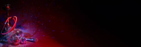 Hookah, glittering mirror disco balls, fir branch, microphone on dark background with red blue lighting. Copy space. New Year. Christmas. Holiday party. Karaoke bar.  Exstra wide banner backgroundの写真素材