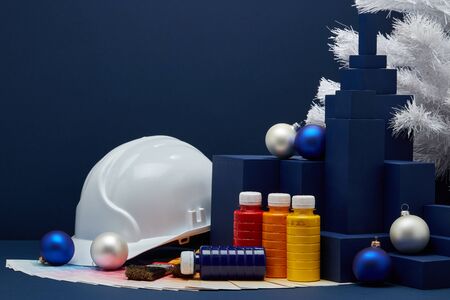 Construction hard hat, color palette guide, paint brushes, Christmas ornaments, white fir tree on...