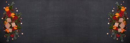 Christmas decorations, gift boxes, mandarins with leaves, red berries, fir branches and cones on dark background. Top view with copy space.  Christmas. New Year. Extra wide panorama banner backgroundの写真素材