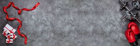 Dumbbells, boxing gloves, gift boxes on grey background. Top view with copy space. Valentine's Day card.   Fitness, sport and healthy lifestyle concept. Extra wide panorama banner backgroundの写真素材
