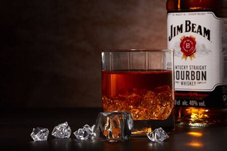 St.Petersburg, Russia - December 2019 - Bottle of Jim Beam bourbon whiskey and glass with drink and ice  on wooden table on brown background with copy space. Kentucky straight bourbon whiskeyのeditorial素材